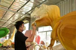 Ένας επιδέξιος τεχνίτης φαναριών ζωγραφίζει στο χέρι ένα μεγάλο φανάρι δεινοσαύρου στο εργαστήριο, αναδεικνύοντας την εξαιρετική λεπτομέρεια και την παραδοσιακή διαδικασία κατασκευής φαναριών.