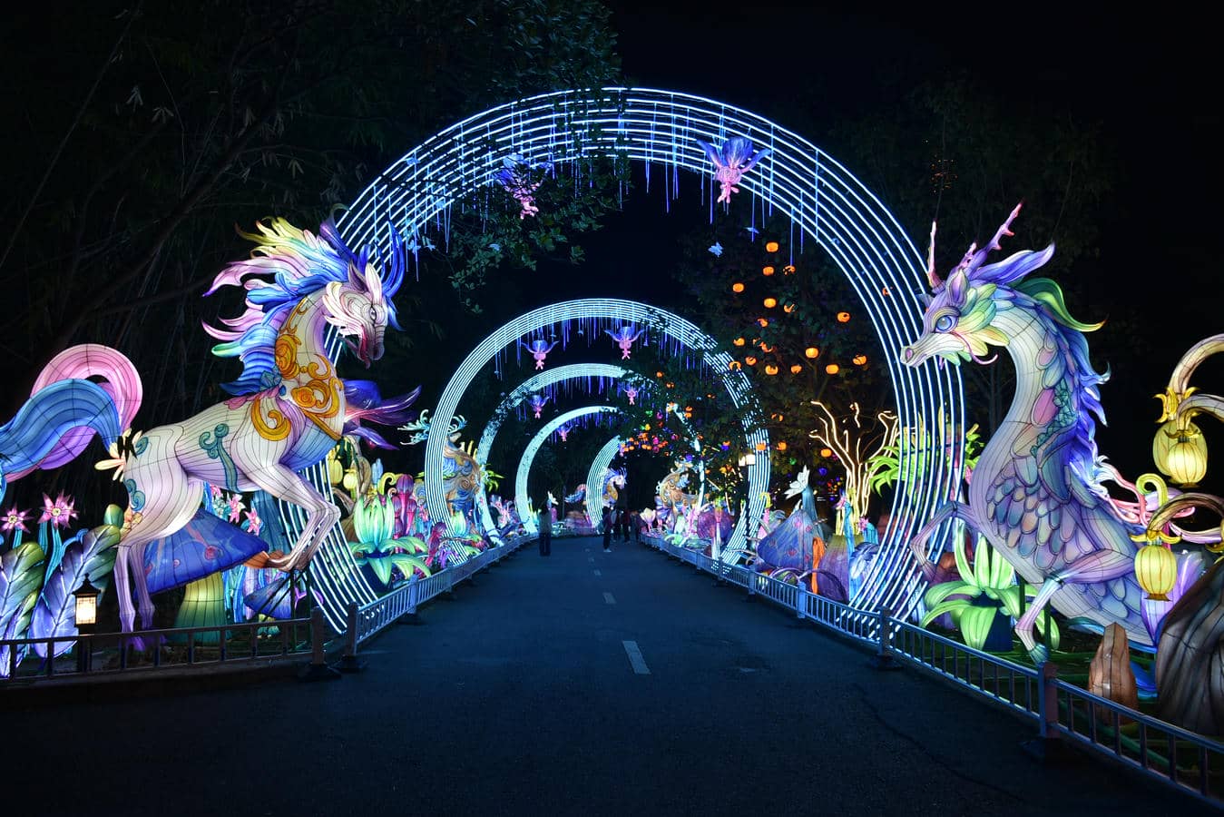 Visitors enter an outdoor park light show through illuminated dragon lantern arches at night