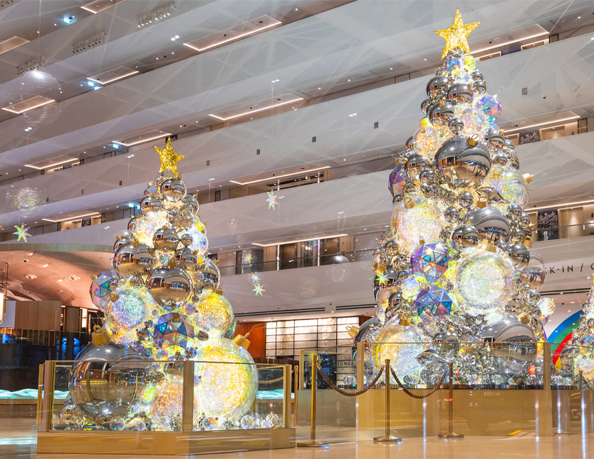 Two large silver mirror Christmas tree decorations inside a mall, with colorful lights and reflective ornaments creating a dazzling holiday atmosphere.