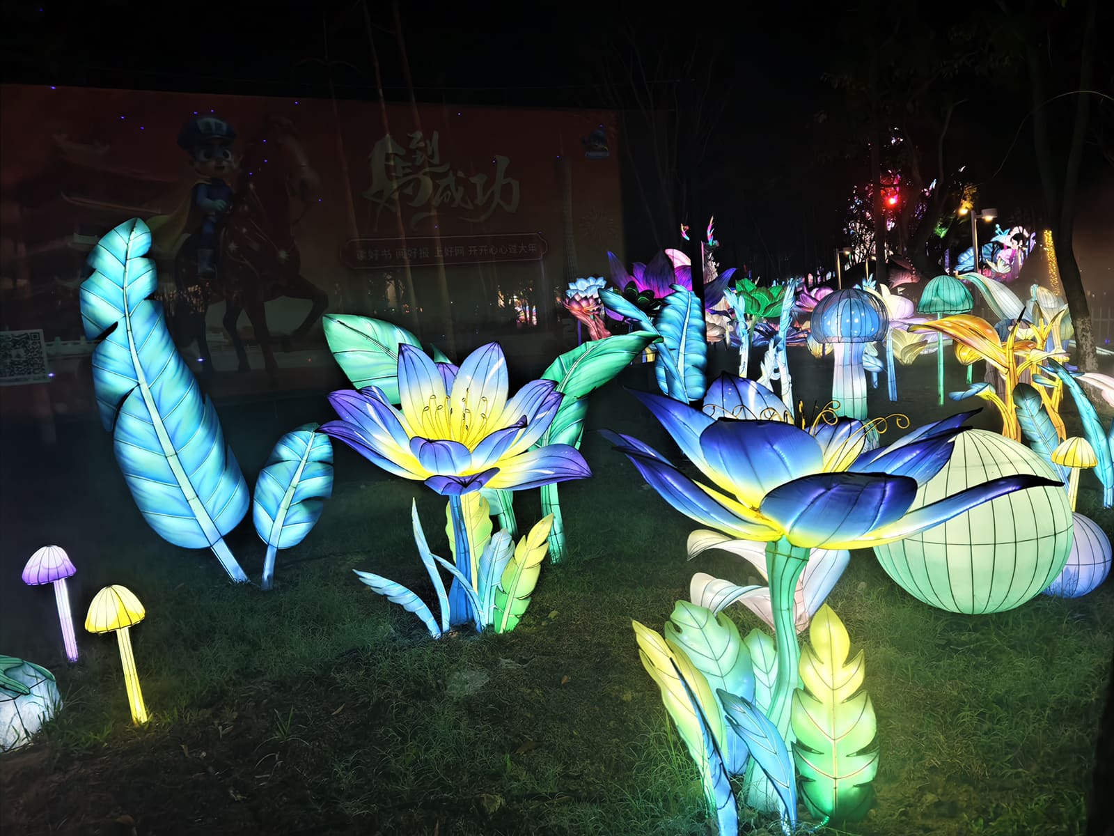 Illuminated flowers, leaves, and mushroom lanterns arranged across an outdoor lawn