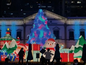 A festive Christmas light display created for the Macau municipal light festival project, featuring a large illuminated Christmas tree, gift boxes, snowman decorations, and holiday lighting in front of a municipal building.