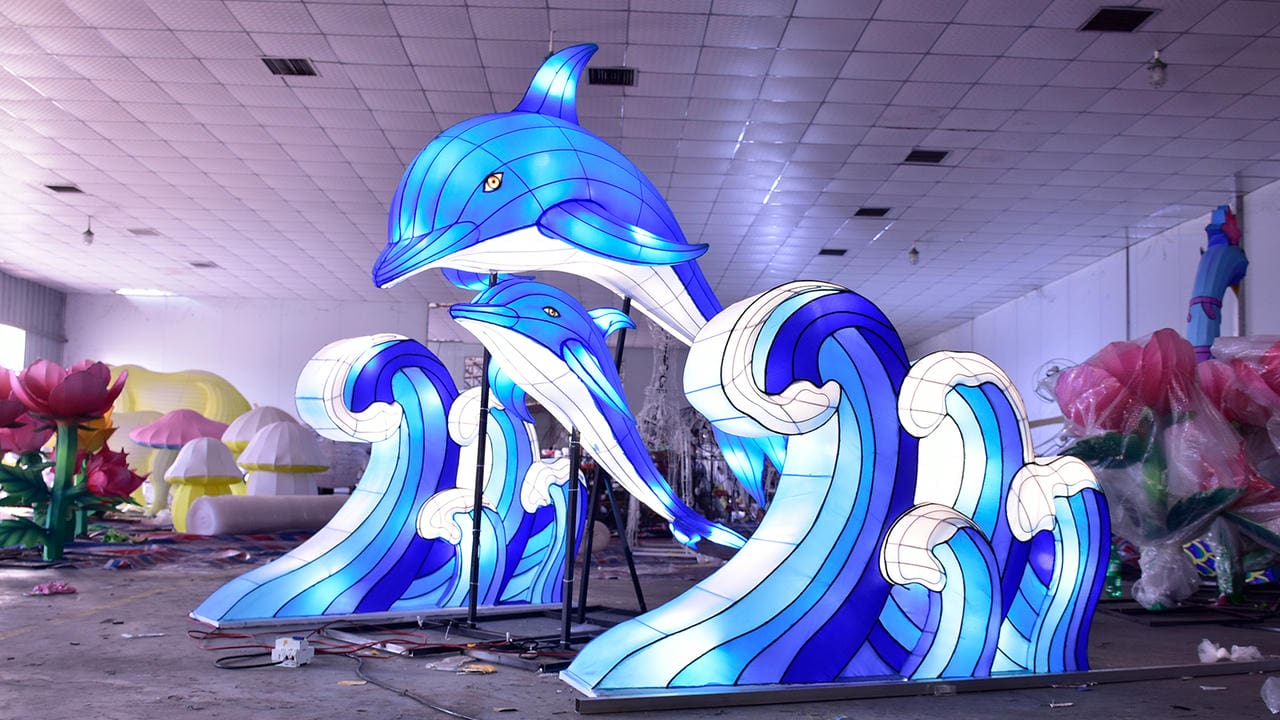 Illuminated blue dolphin lanterns rising above stylized ocean waves in an indoor work area