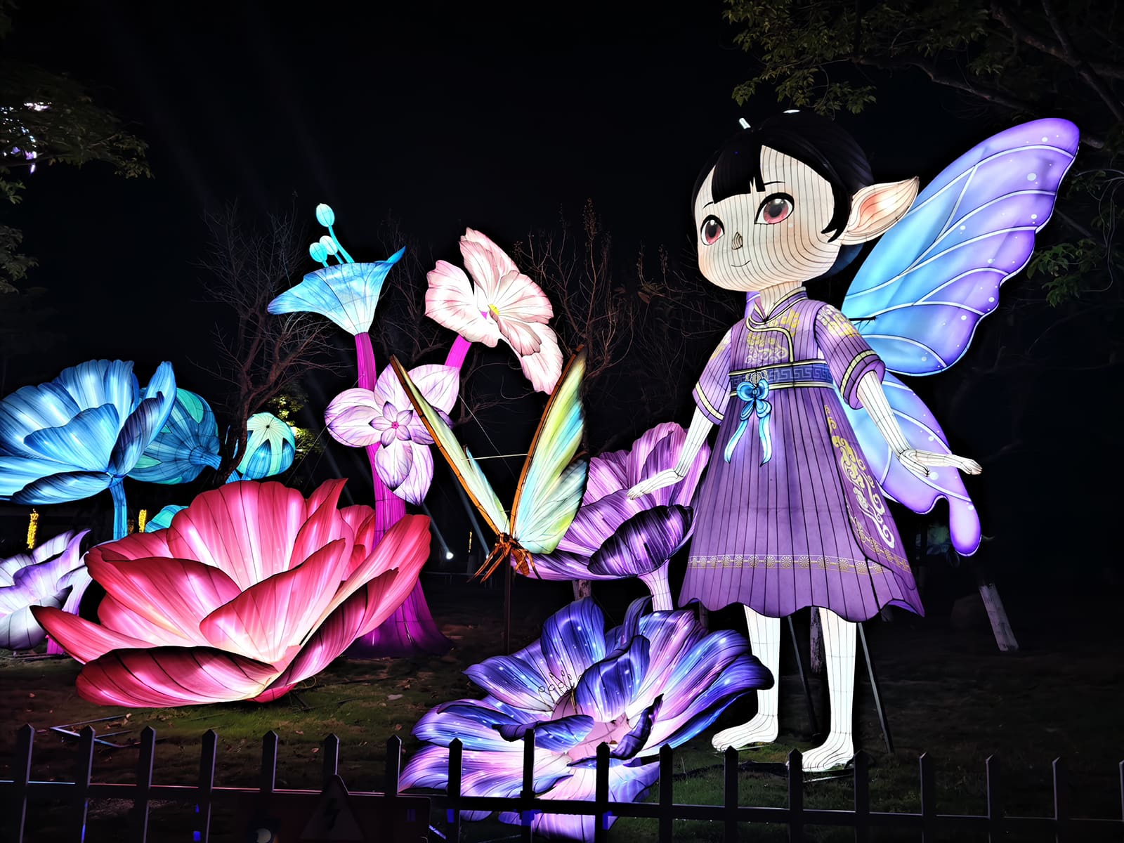 Large winged fairy lantern figure standing among illuminated flowers